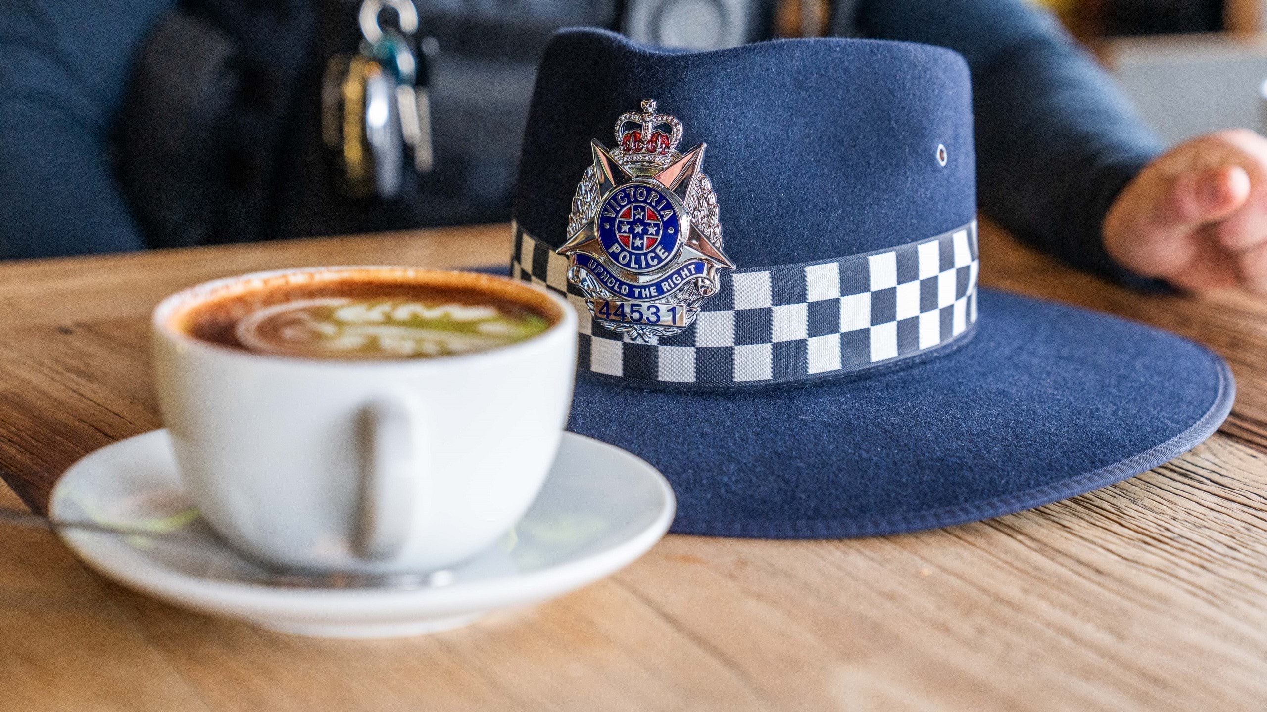 Victoria Police branded uniform hat resting on a wooden table next to a cup of coffee perhaps in a cafe