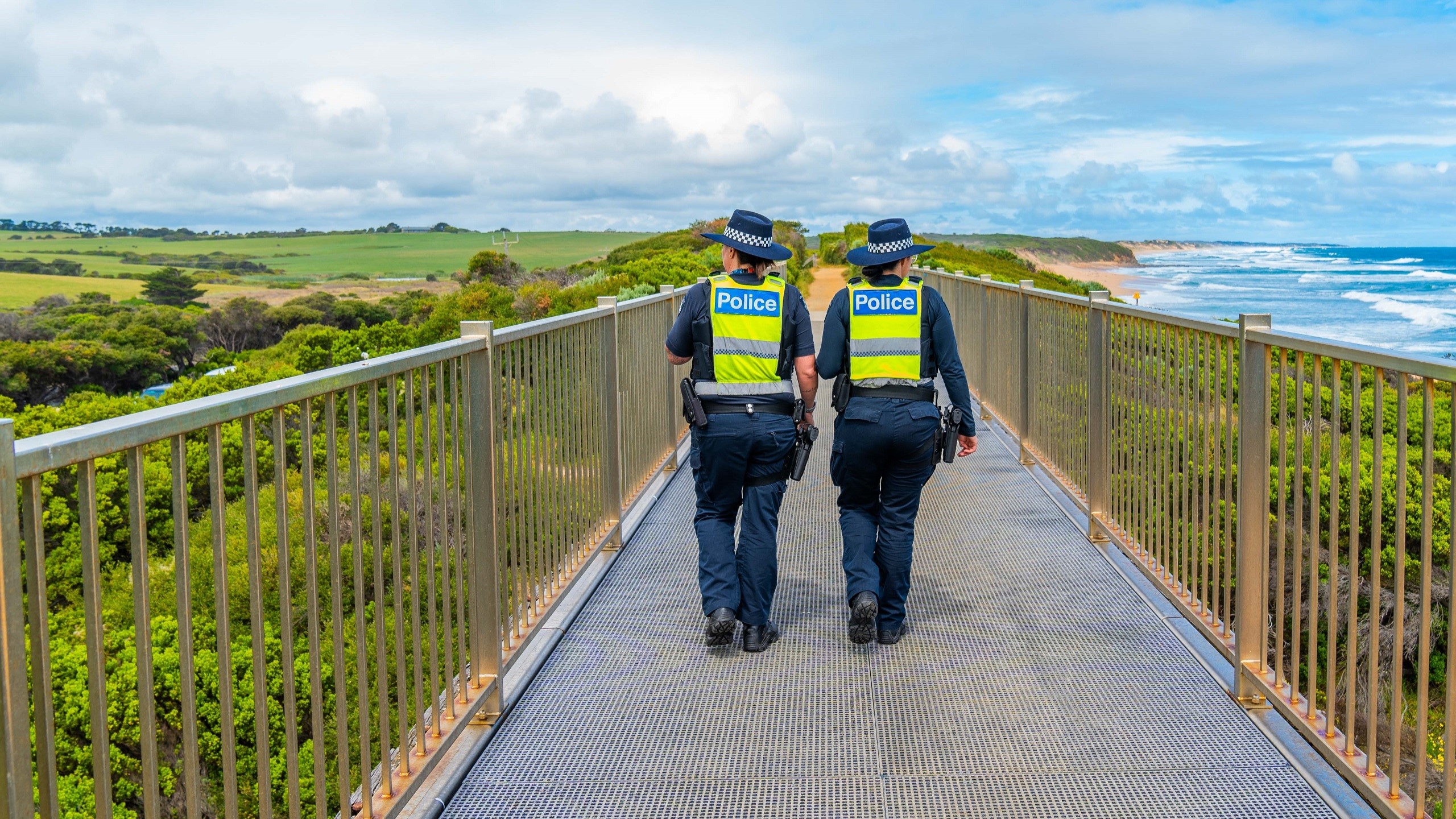 Supporting Victoria Police employee wellbeing Two police officers walking along a jetty with green brushland to their left and the ocean plus sand dunes to their right