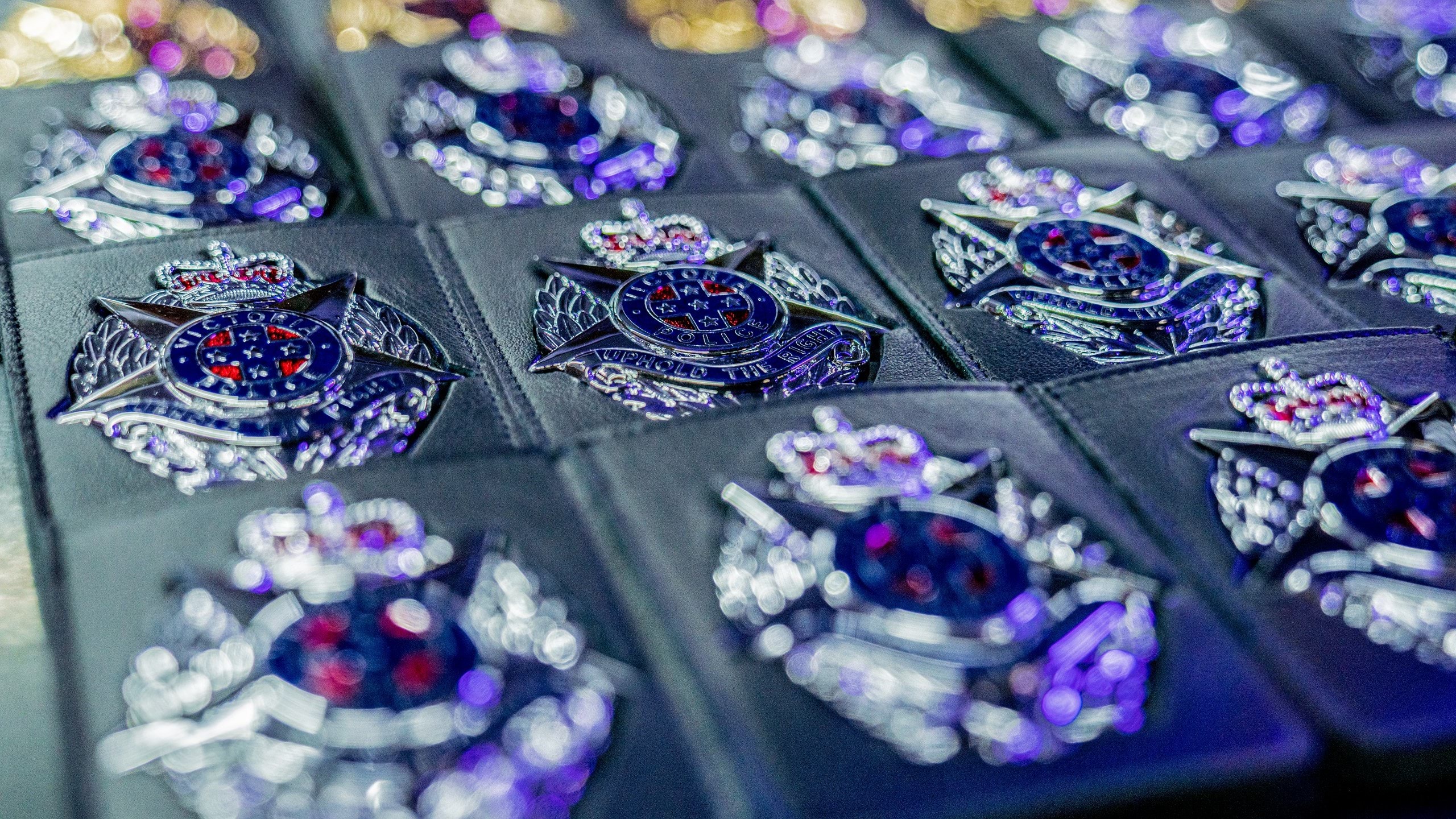 Display of silver police badges in their black, pocket-size holders lined up on display. Badge image is a silver star on an oval shaped background, with a crown resting on the top point of the star. Text on the badge reads Victoria Police, Uphold the Right.