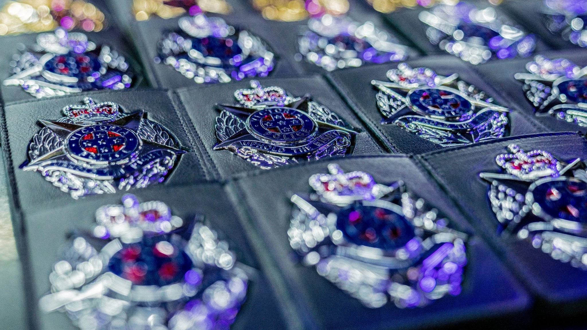 Mental health, resilience and wellbeing in the Police Display of silver police badges in their black, pocket-size holders lined up on display. Badge image is a silver star on an oval shaped background, with a crown resting on the top point of the star. Text on the badge reads Victoria Police, Uphold the Right.