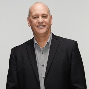 Jim's story Image of current police chaplain smiling at the camera wearing a grey and white pattern shirt with a navy suit jacket on top. Late forties, male with light skin and light, receding hair.