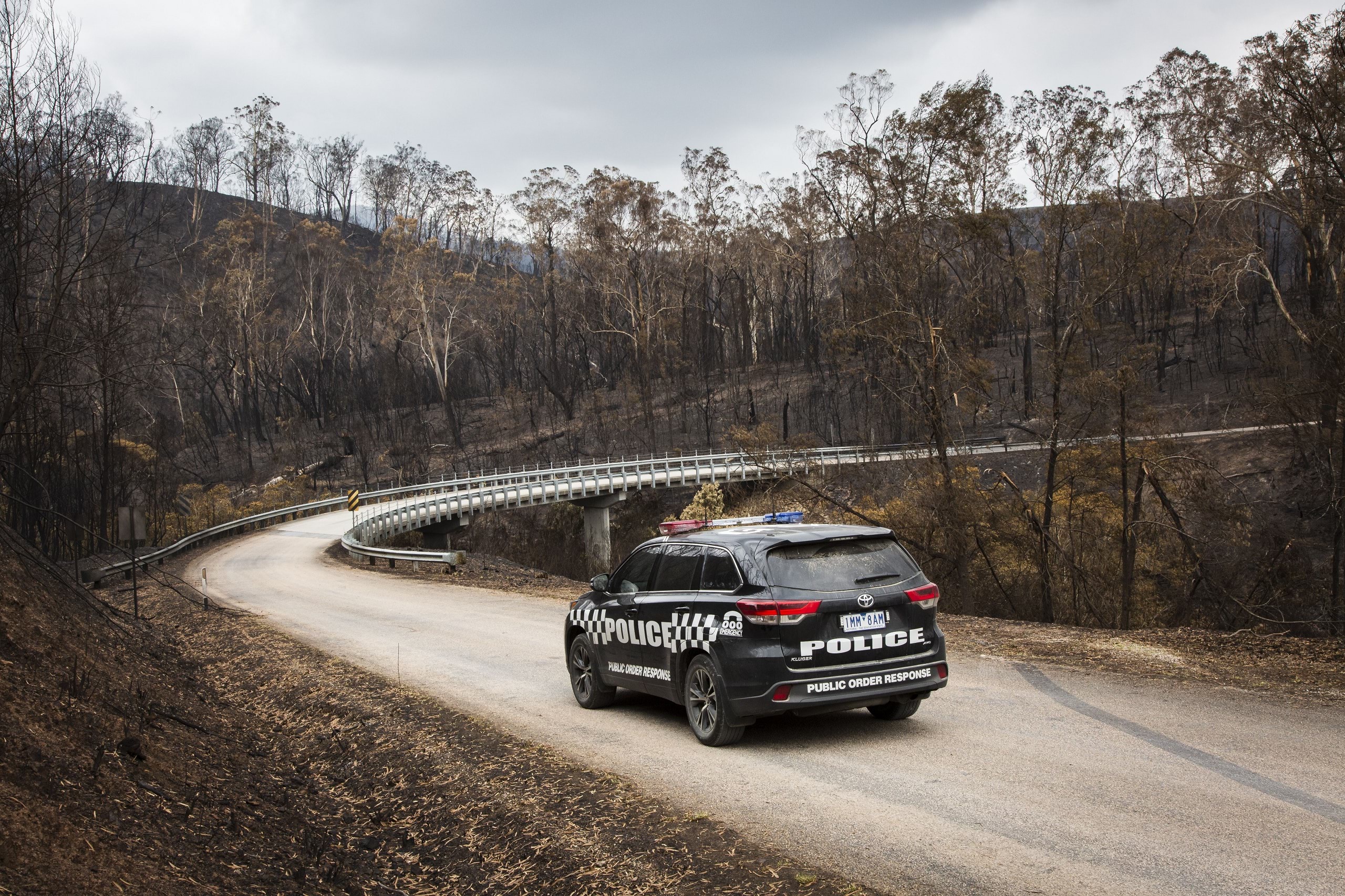 Lone police car driving through bushfire affected disaster zones.