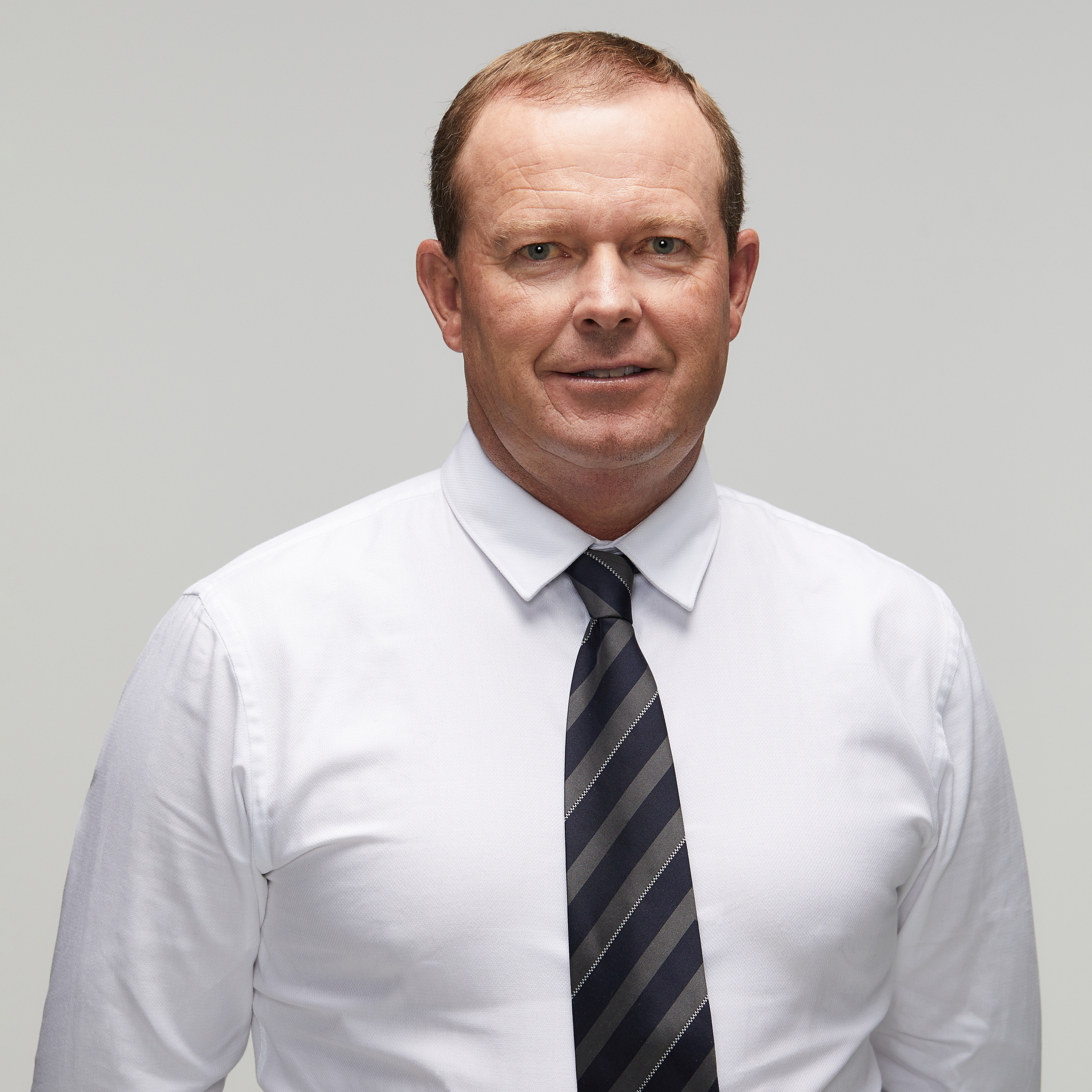 Image of current police officer looking at camera wearing white shirt with black and grey stripped tie; white male late thirties early forties