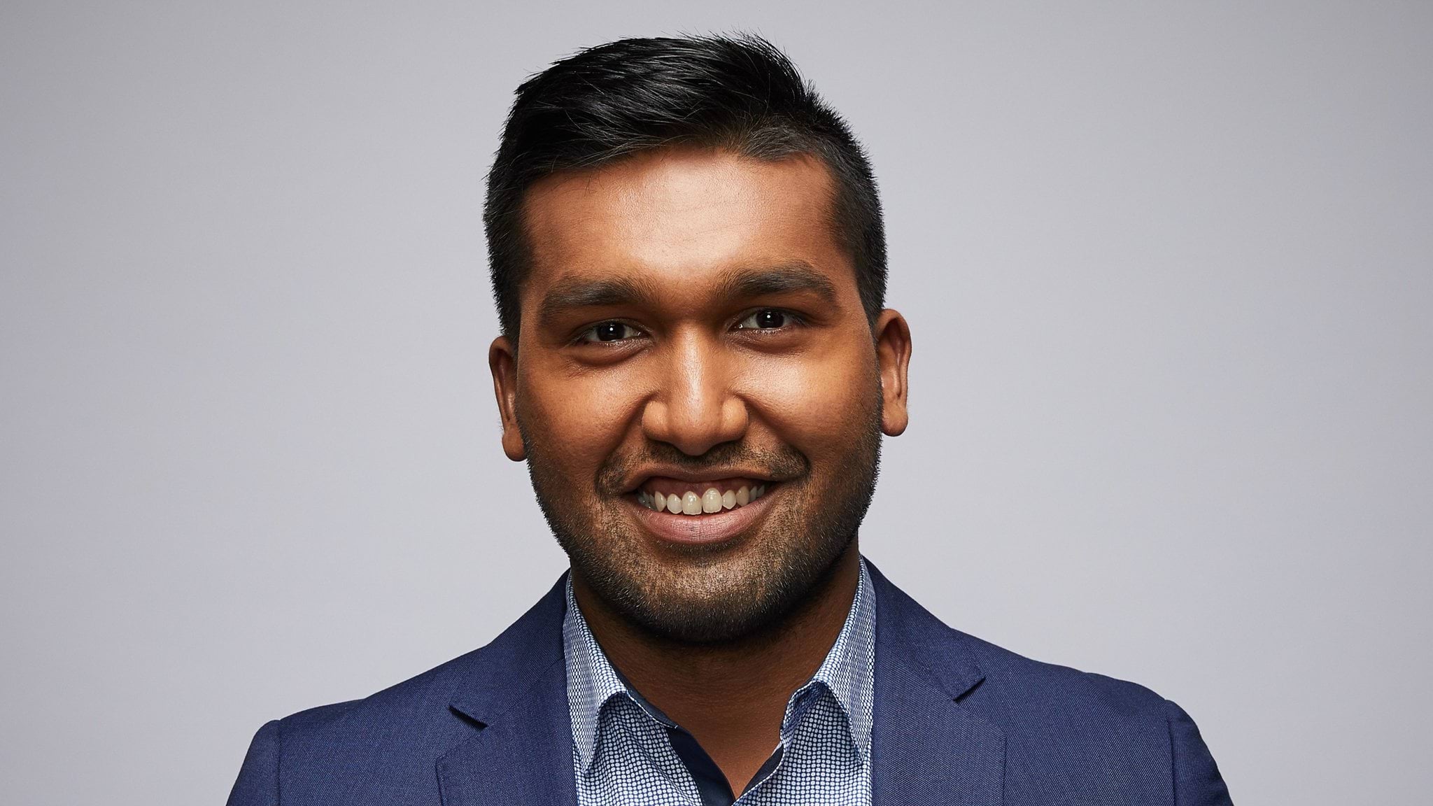 Sean's story Image of current VPS employee looking slightly off camera to the left wearing a light blue shirt with a dark blue suit jacket. Dark skin, slight beard stubble, and black hair